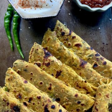 Indian thepla (flatbread) with spicy tomato chutney, yogurt, and green chilies on a dark surface.
