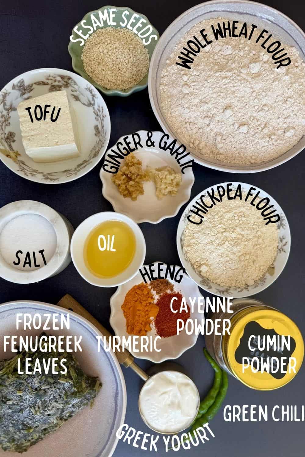 Ingredients for high protein tofu thepla (Indian flatbread) in bowls on a blue background including whole wheat and chickpea flours, frozen fenugreek leaves, tofu, yogurt, and spices.