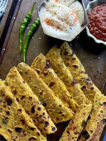 Indian thepla (flatbread) with spicy tomato chutney, yogurt, and green chilies on a dark surface.