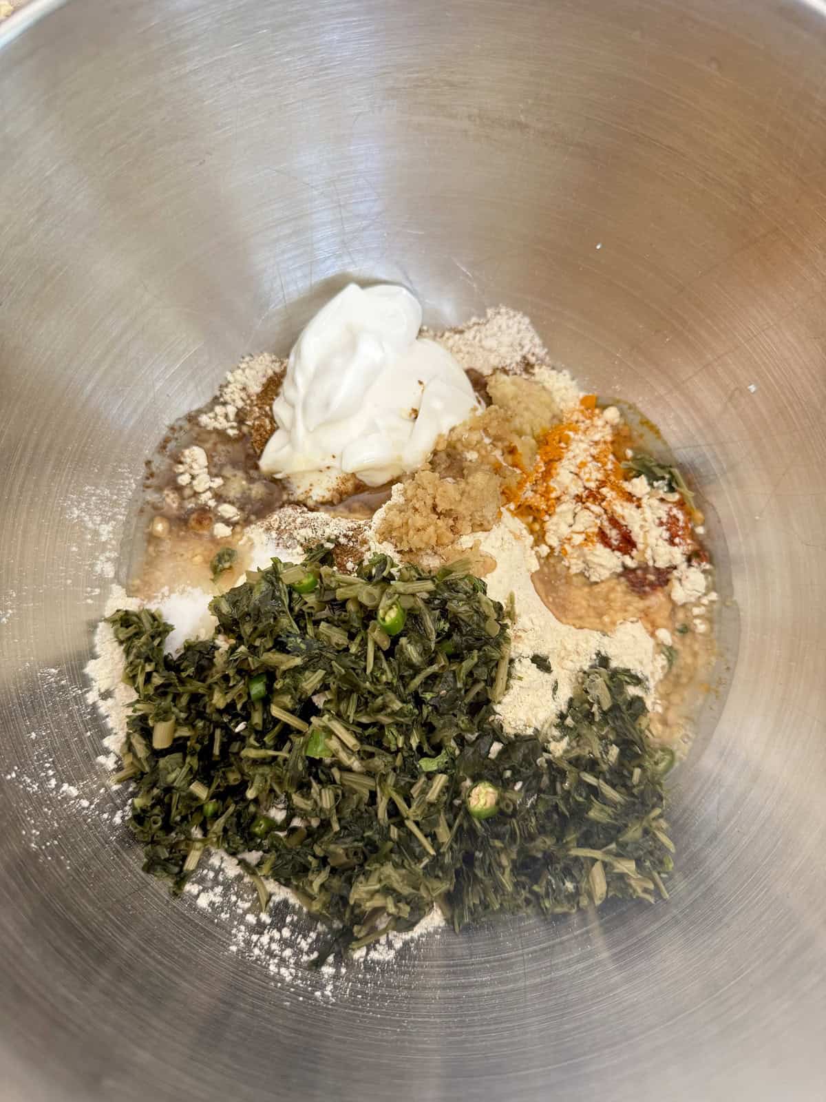 Frozen fenugreek leaves and yogurt along with other ingredients of high protein tofu theplas in a stainless steel mixing bowl.