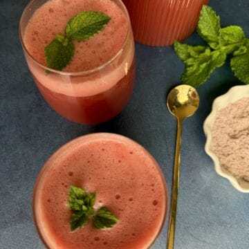 Two glasses of refreshing watermelon mint spritzer with crushed ice, garnished with a fresh mint sprig on a summer table.