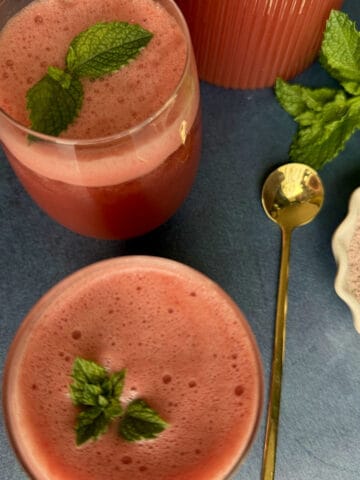 Two glasses of refreshing watermelon mint spritzer with crushed ice, garnished with a fresh mint sprig on a summer table.
