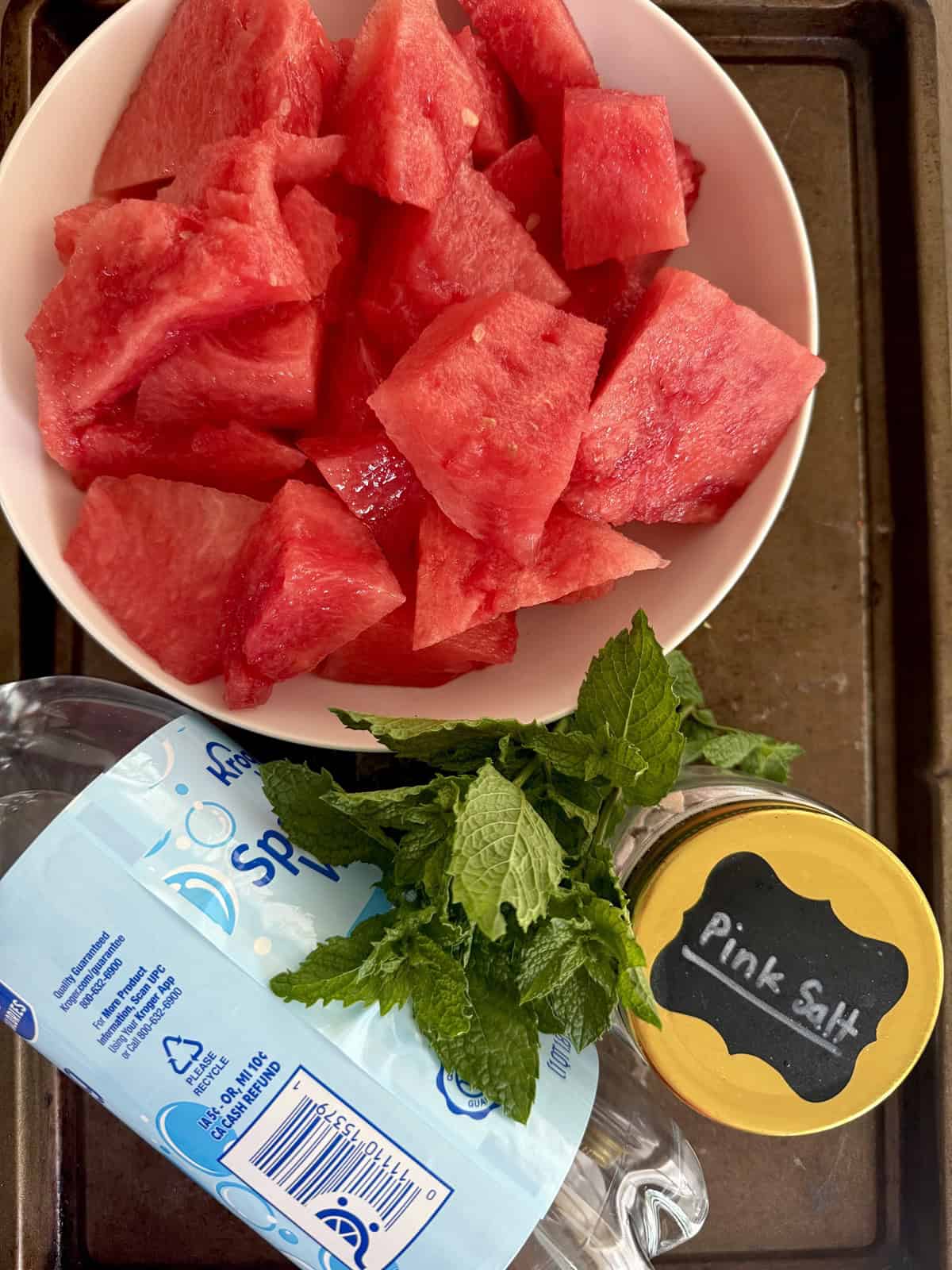 Ingredients for watermelon mint spritzer including watermelon pieces, pink salt, mint, and fizzy sparkling water.