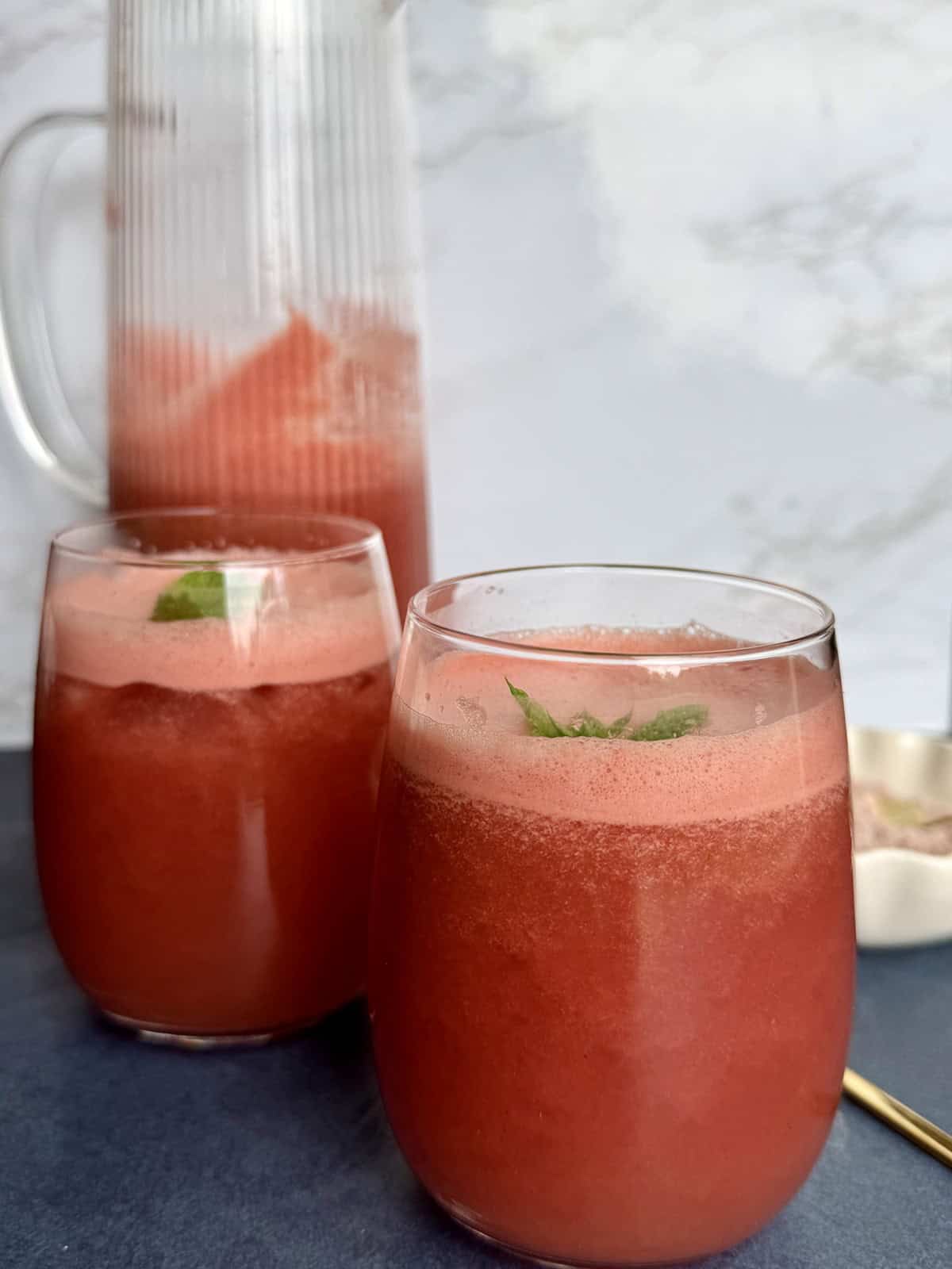 Two glasses of refreshing watermelon mint spritzer with crushed ice, garnished with a fresh mint sprig on a summer table.