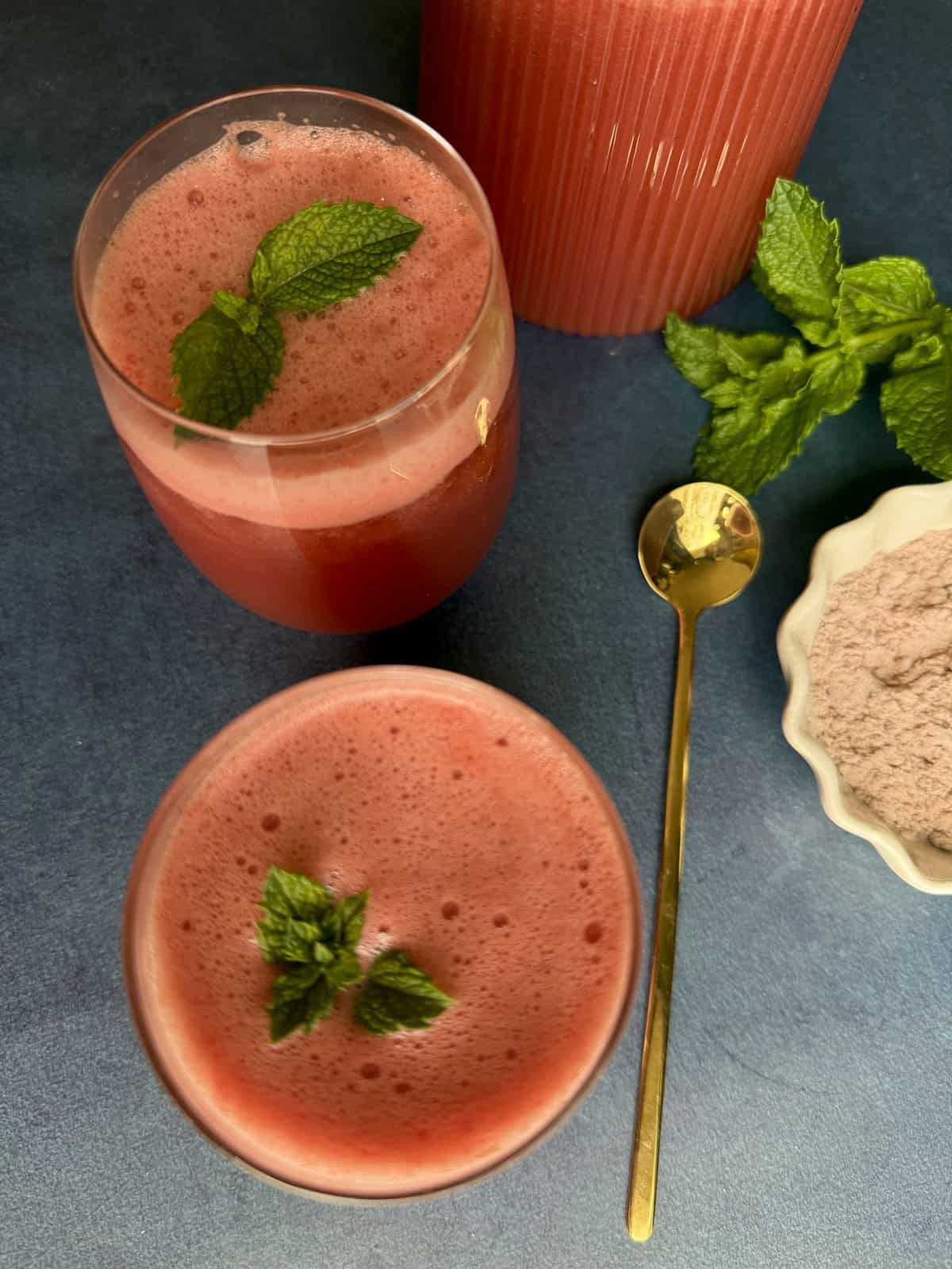 Two glasses of refreshing watermelon mint spritzer with crushed ice, garnished with a fresh mint sprig on a summer table.