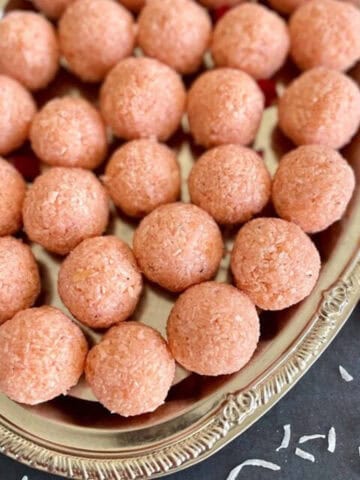 Close-up of rose coconut ladoos on a decorative silver platter.