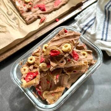 Nut-free high protein chocolate yogurt bark broken into pieces in a freezer safe glass container with SunButter swirl and crispy cereal and strawberry topping.