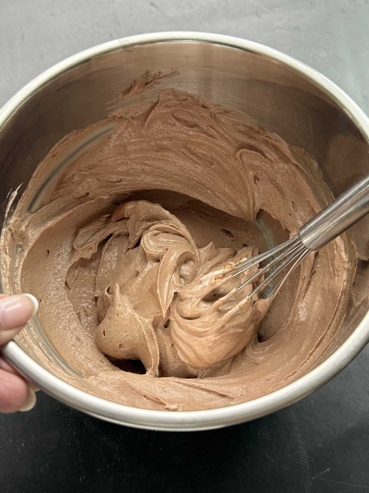 Whisking plain Greek yogurt and chocolate protein powder in a bowl with maple syrup and cocoa powder to make a high-protein frozen yogurt bark base.