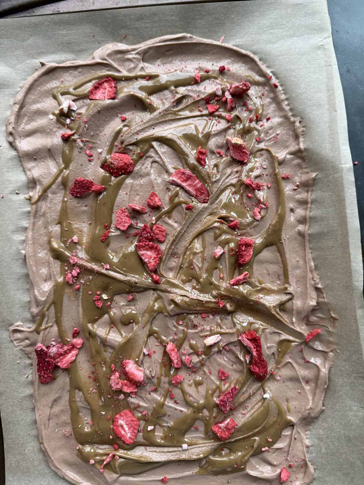 Adding freeze dried strawberries onto chocolate SunButter yogurt bark before freezing.