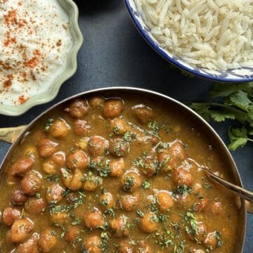 Punjabi kala chana curry, black chickpea curry in a onion-tomato masala served in a stainless steel bowl with basmati rice on the side.
