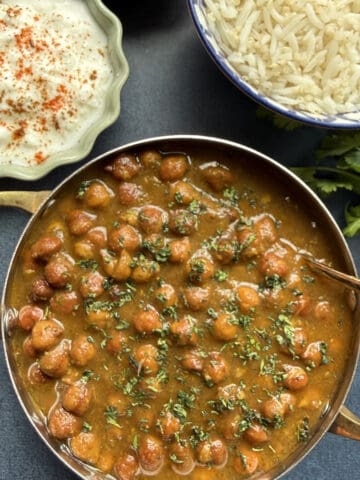 Punjabi kala chana curry, black chickpea curry in a onion-tomato masala served in a stainless steel bowl with basmati rice on the side.