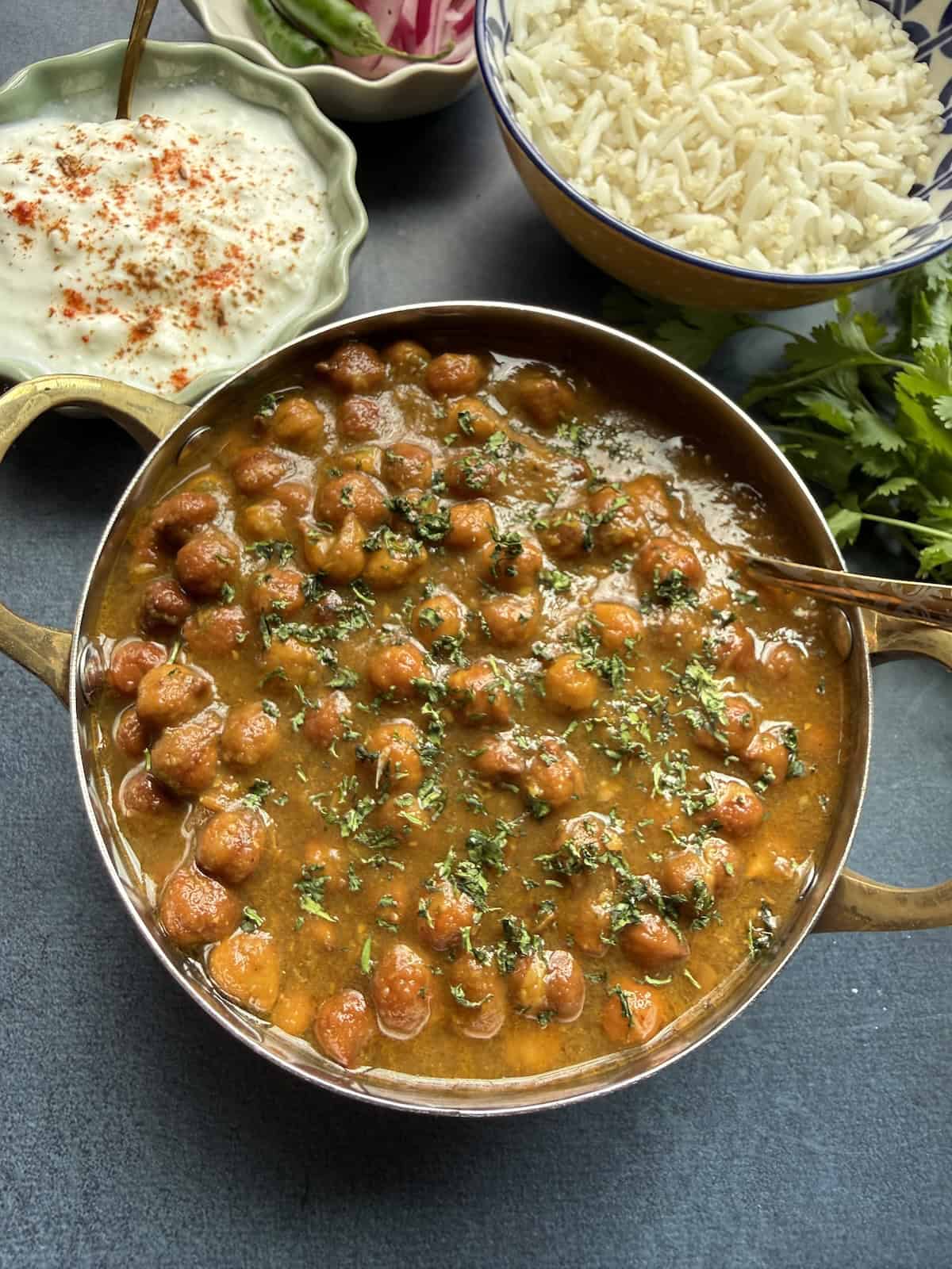 Punjabi kala chana curry, black chickpea curry in a onion-tomato masala served in a stainless steel bowl with basmati rice on the side.