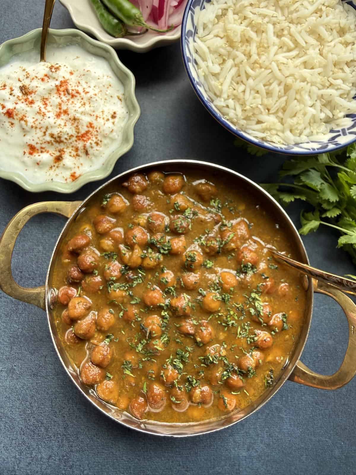 Punjabi kala chana curry, black chickpea curry in a onion-tomato masala served in a stainless steel bowl with basmati rice on the side.