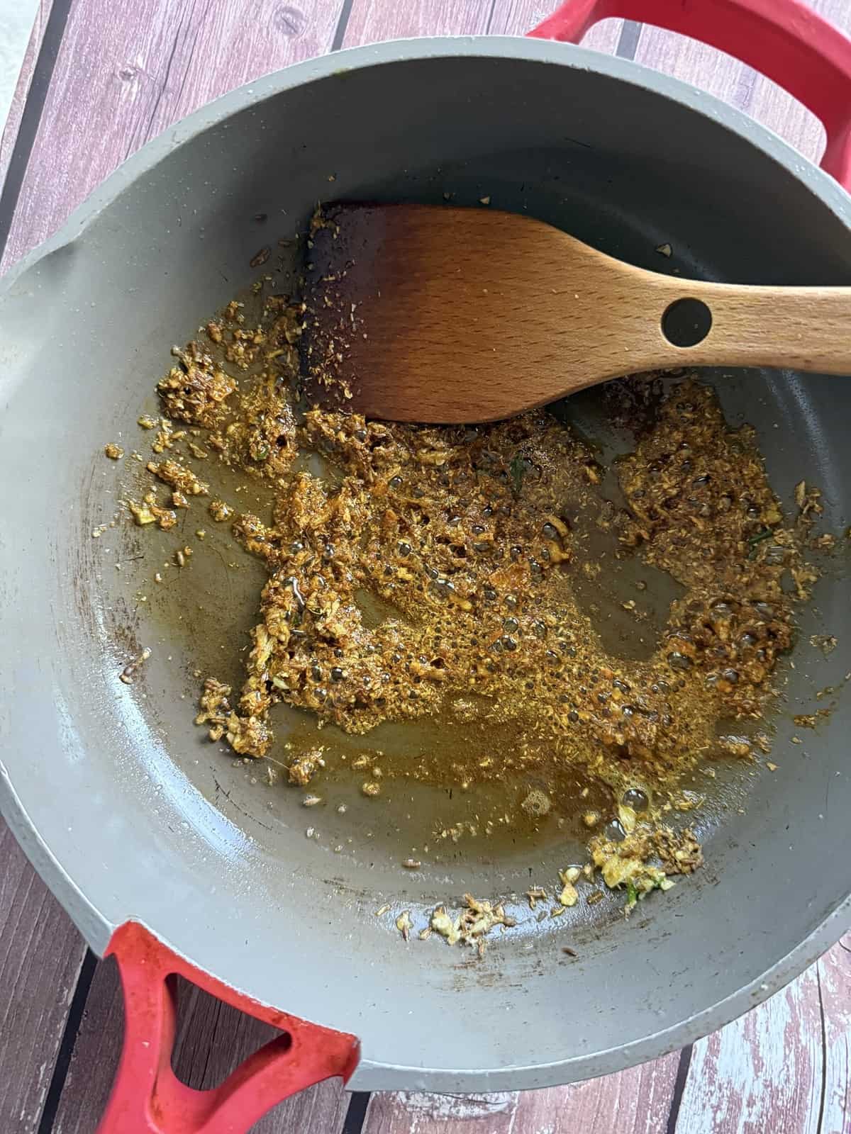 Ginger garlic and green chili paste and spices being sautéed in a non-stick pan with a wooden spatula.