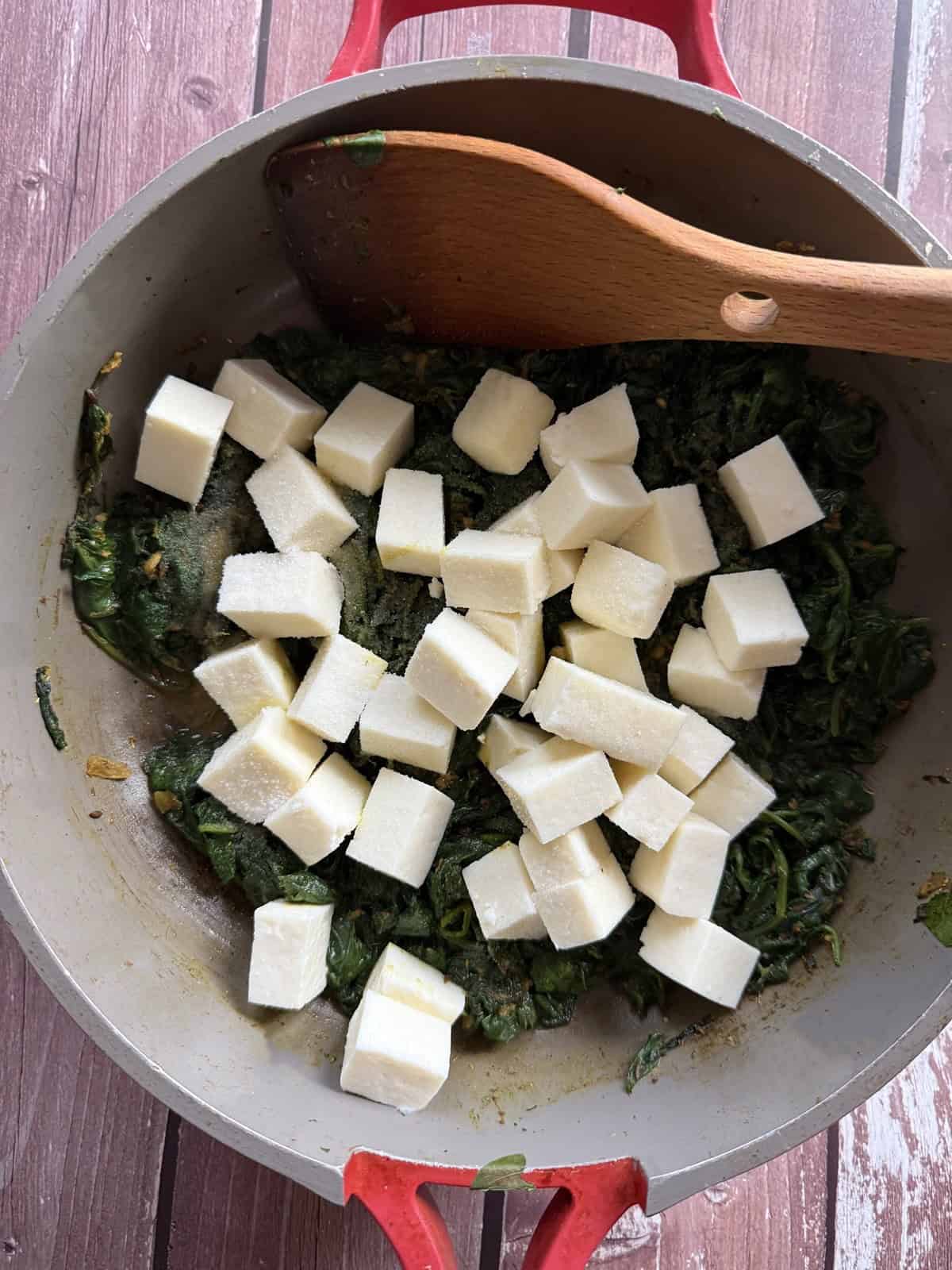 Paneer cubes sprinkled with salt on top of cooked spinach in a ceramic non-stick pan for easy 20-minute palak paneer.